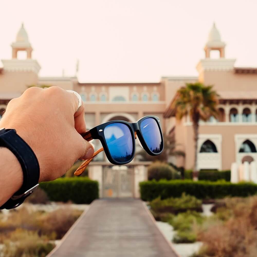 hand holding polarized sunglasses in front of a hotel