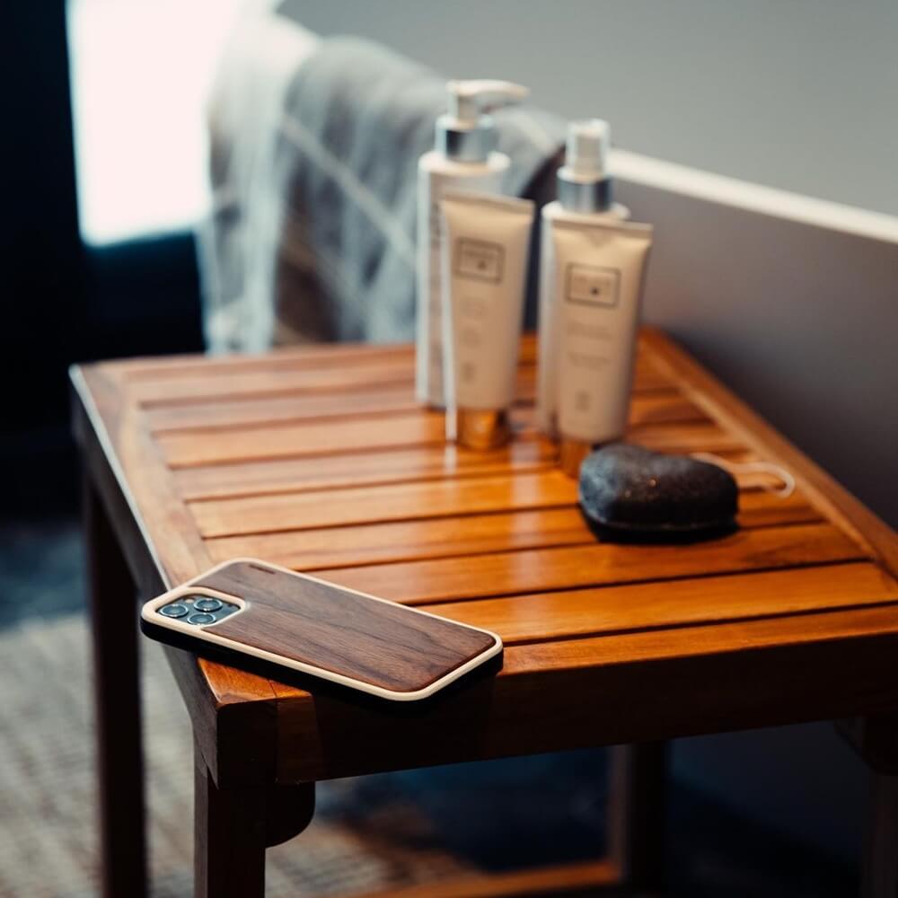 Close-up of iPhone 13 with a walnut iPhone wooden case on a table, alongside refillable lotion bottles