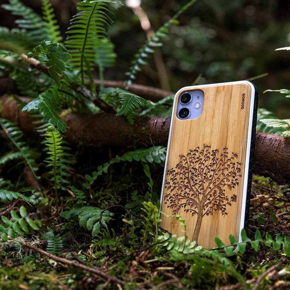 wooden iPhone 11 case with a tree design on the back, resting on a log in a forest