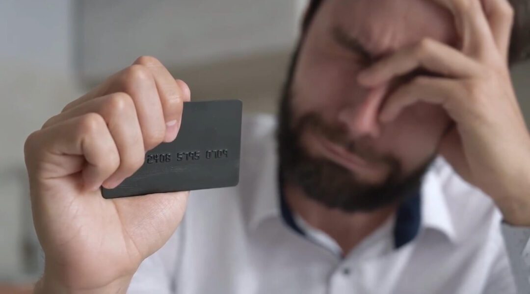 A man looking stressed or concerned while holding a credit card, which highlights the need for an RFID-blocking wallet in Canada to protect against potential digital theft