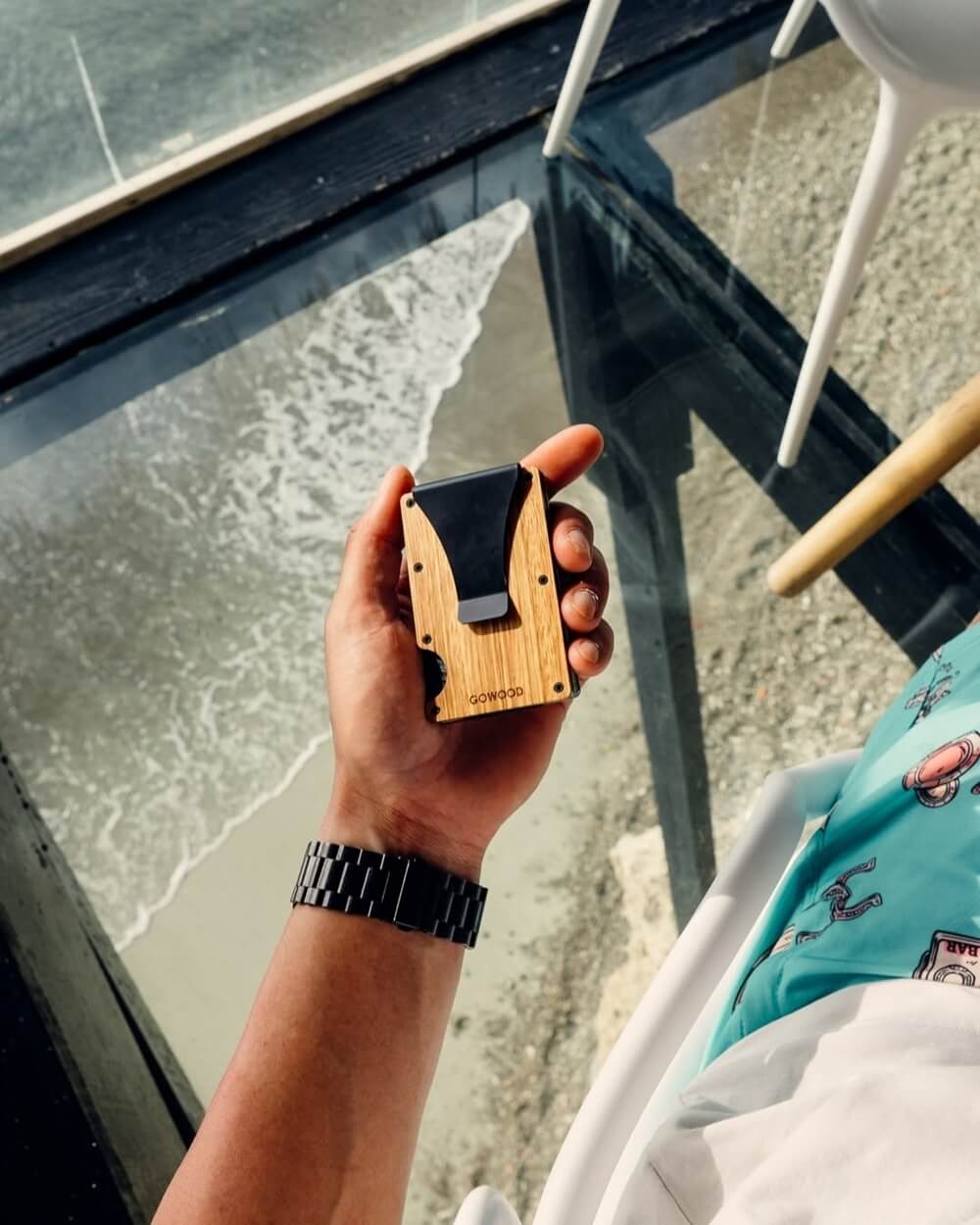 A person's hand holds a light wooden wallet with a black money clip, which could be an RFID-blocking wallet