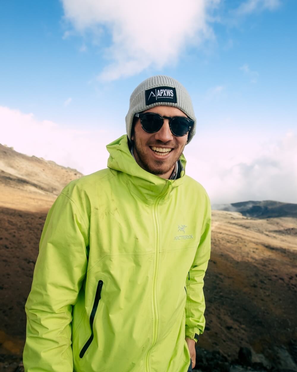 A smiling man in a lime green jacket, grey beanie, wearing sunglasses in autumn