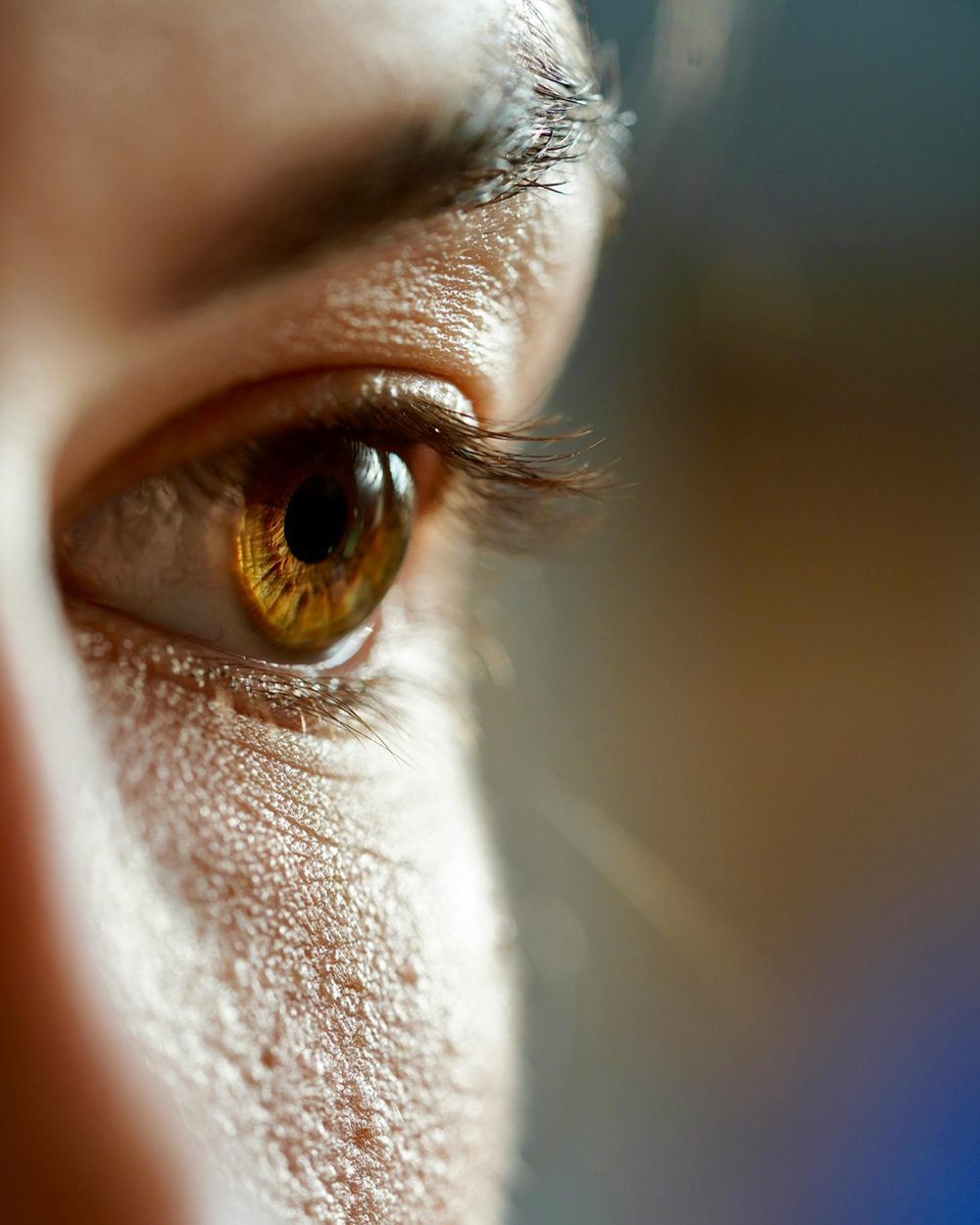 A very close-up, detailed side profile of a human eye with warm brown and amber tones in the iris