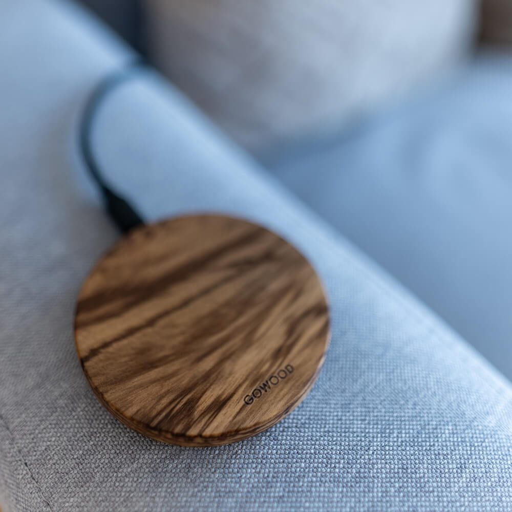 A GoWood brand wooden wireless charger resting on a gray upholstered sofa armrest