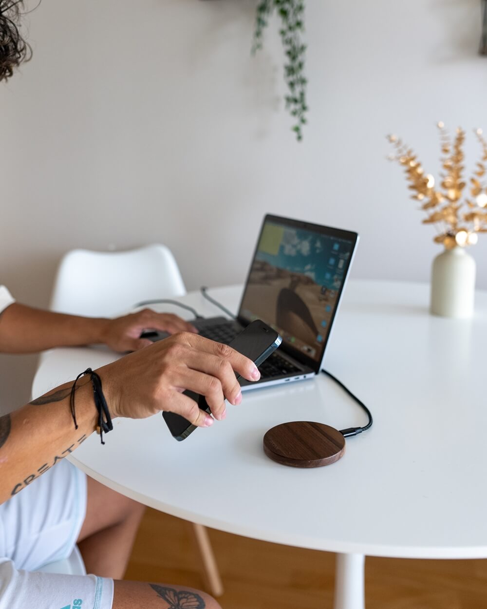 A person's arm with a tattoo holding a phone, with wooden wireless chargers on a white desk