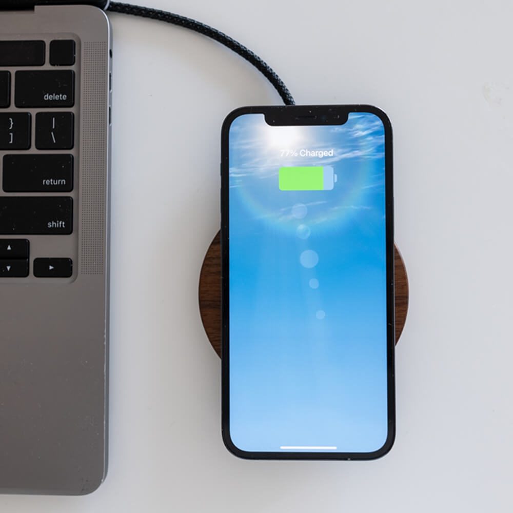 A smartphone displaying 77 Charged on a wooden wireless chargers next to a laptop