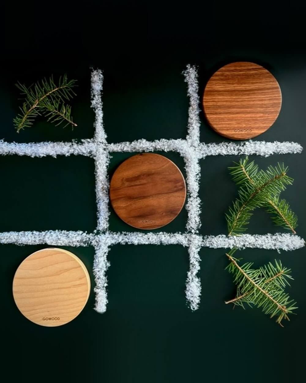 A tic-tac-toe game laid out with three round wooden coasters as pieces, outlined with white powder, and decorated with pine sprigs