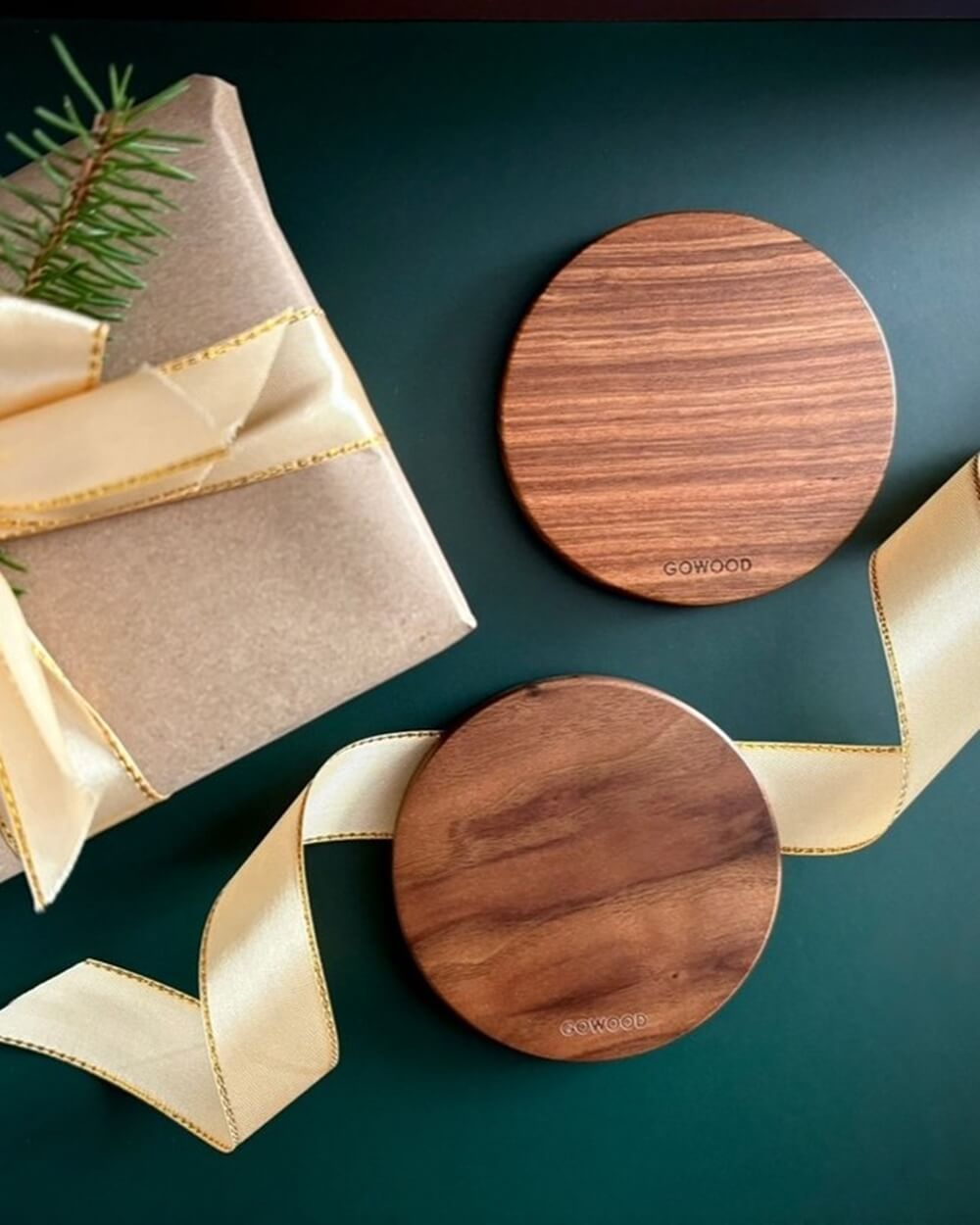 Two GoWood wooden chargers on a dark green surface, alongside a gift wrapped in kraft paper